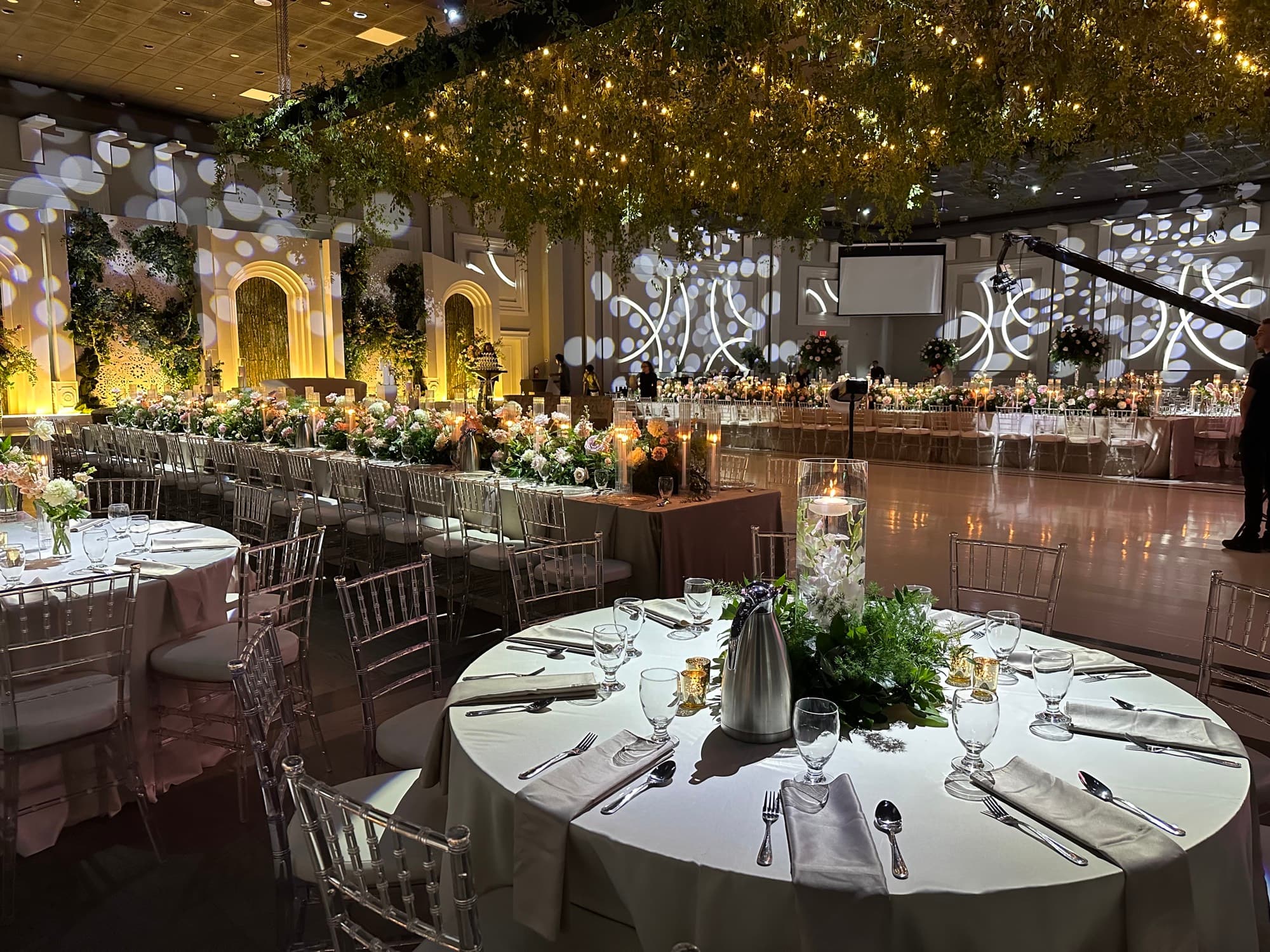 Greenery canopy strung with lights above a long floral head table and open dance floor at Palacio Event Centre