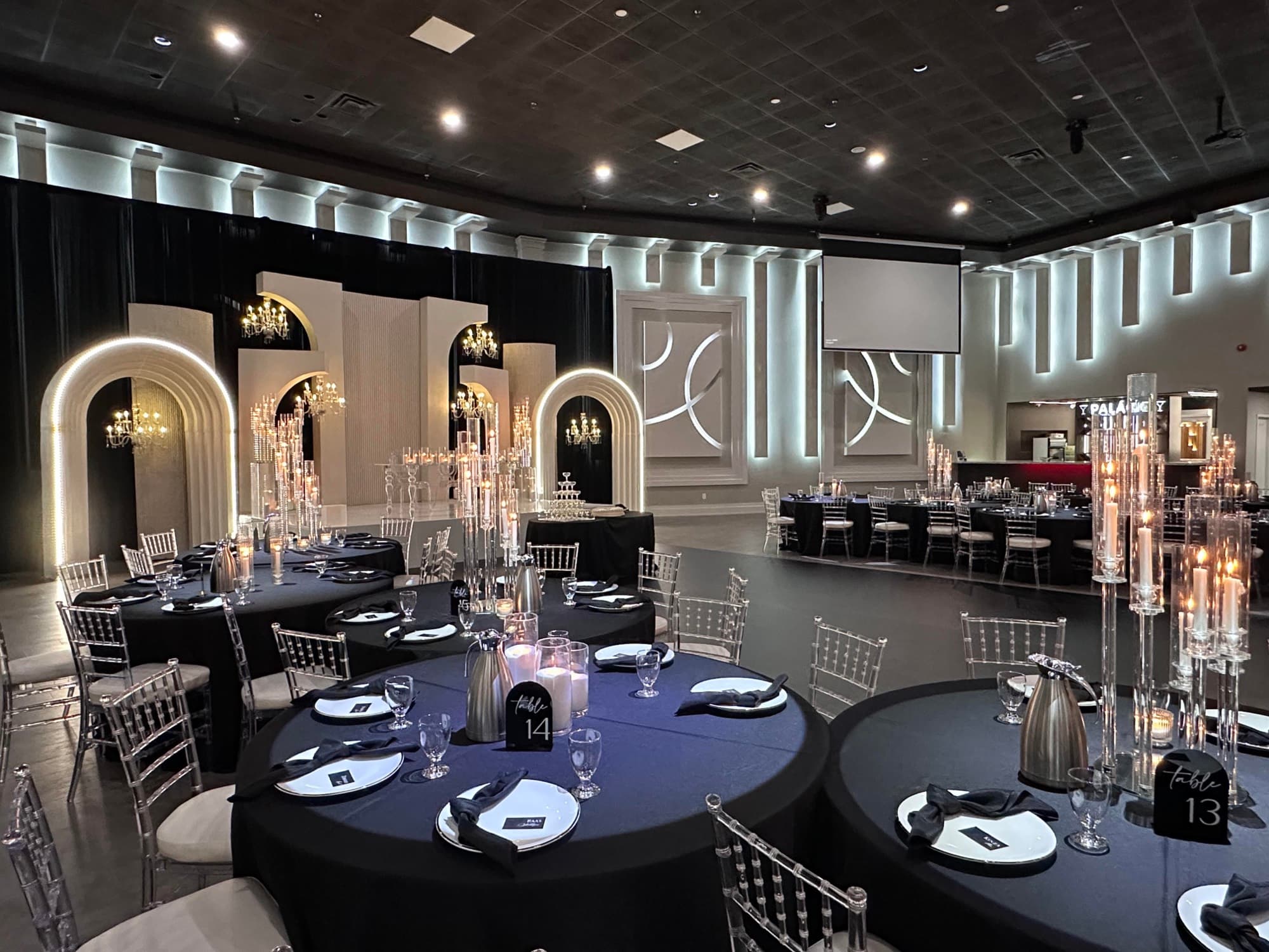 Reception room at Palacio Event Centre set with black linens, tall glass candelabras and an illuminated arched backdrop